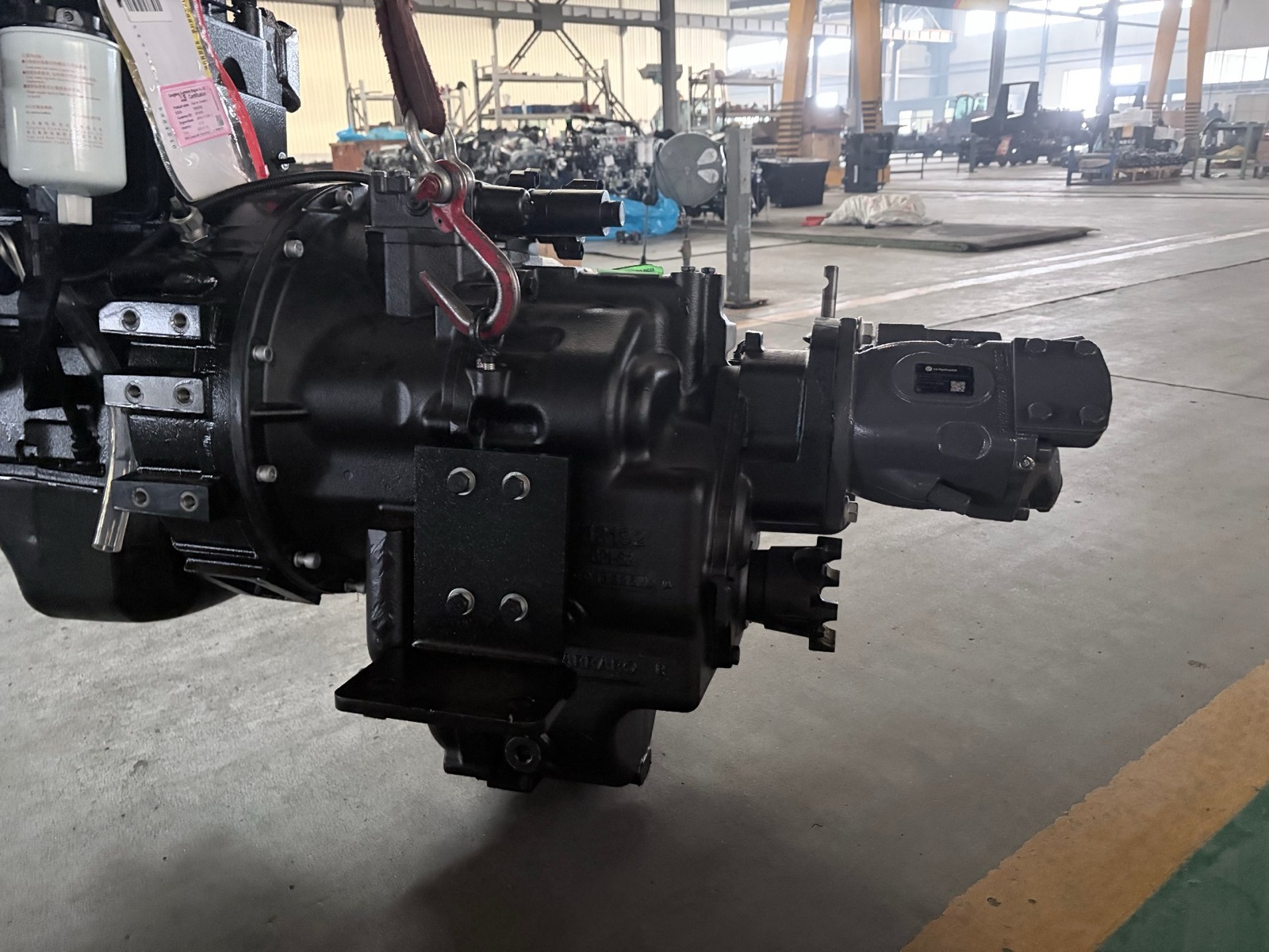 A Carraro axle and powershift transmission assembly hanging from a crane hook on the AOLITE assembly floor, waiting to be fitted to a backhoe loader