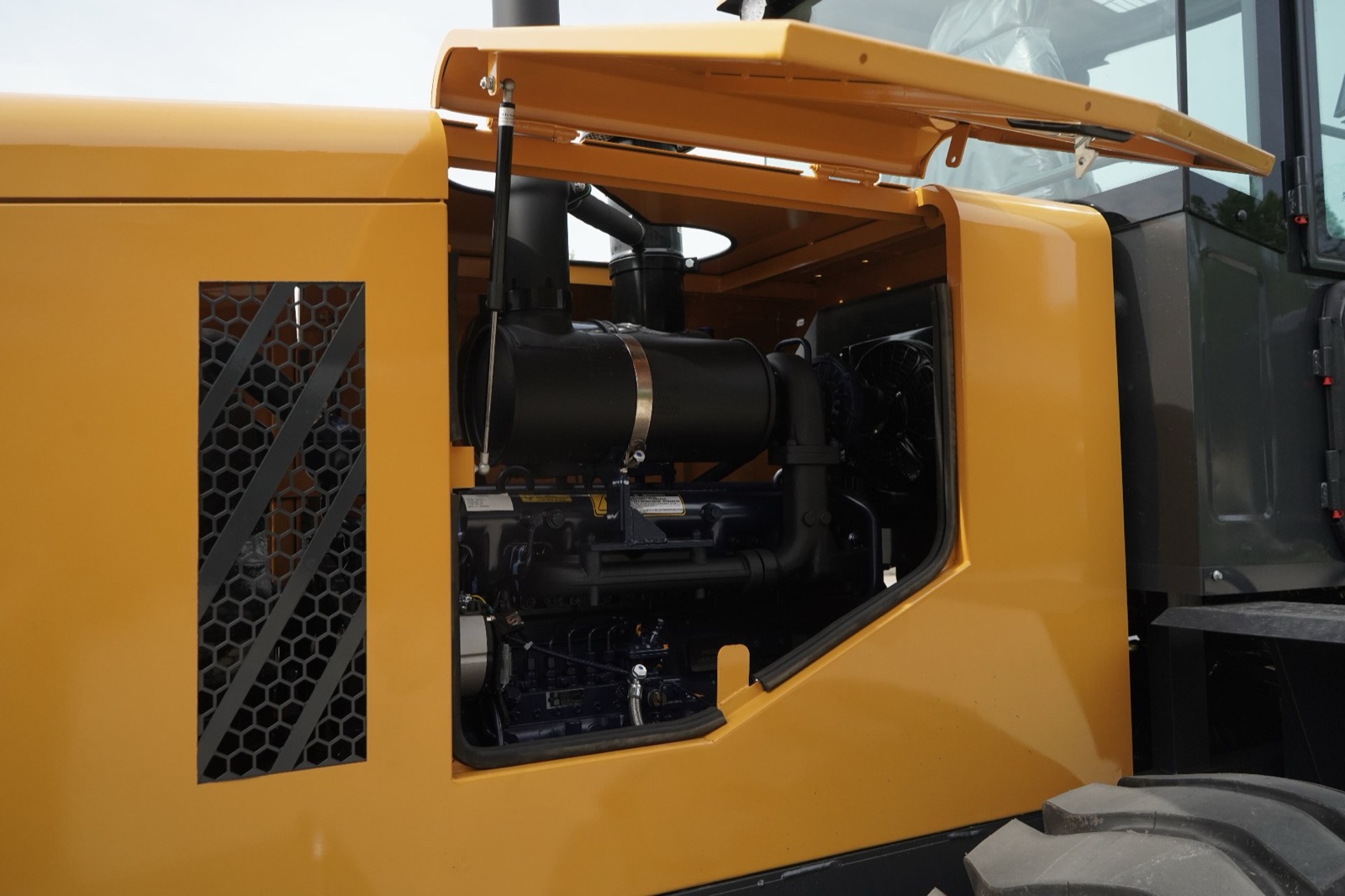 Engine bay of a new backhoe loader with the side panel open, showing the air filter housing, exhaust routing and cooling fan before delivery