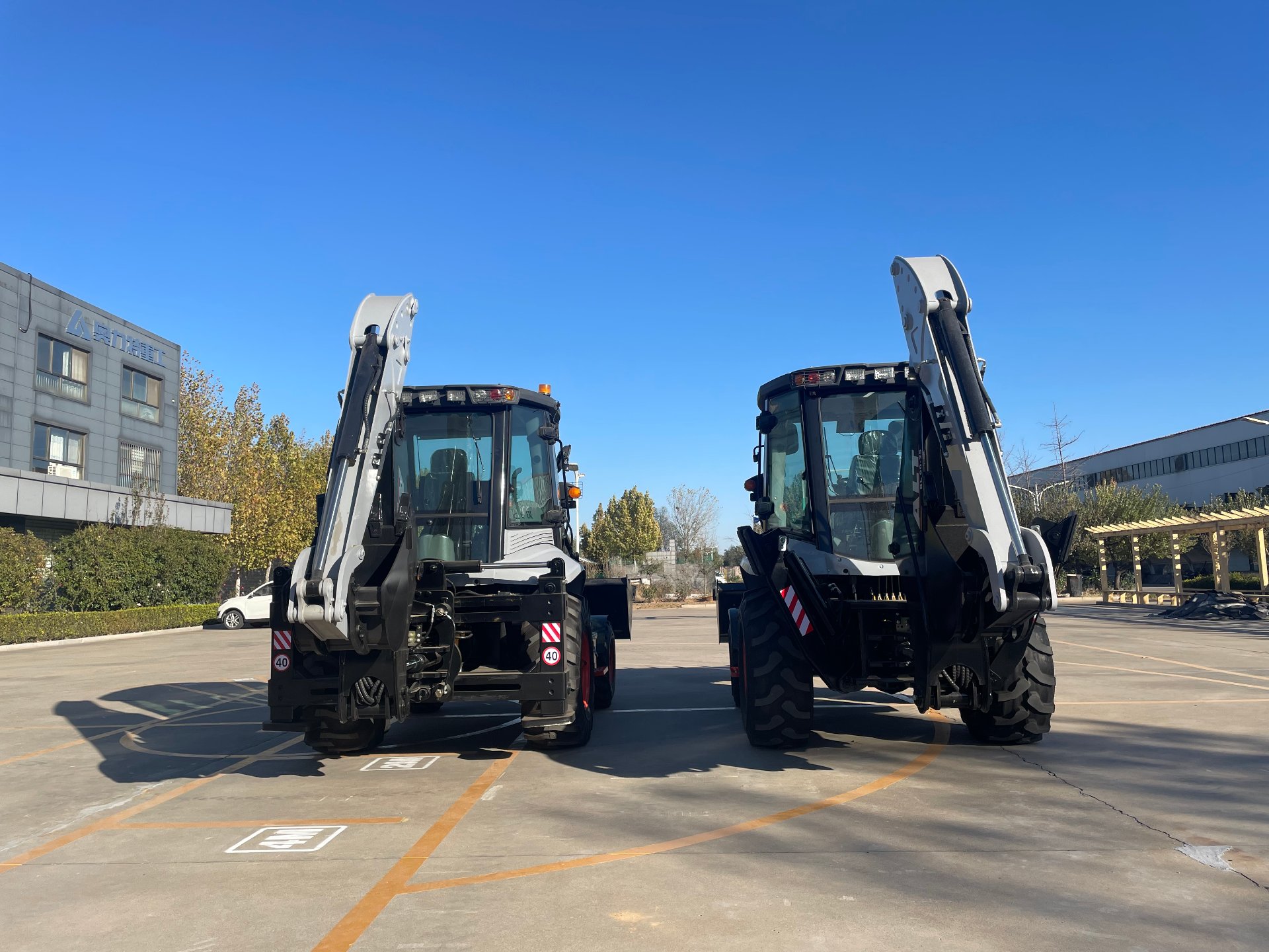 Two BL80-25 backhoe loaders lined up at the factory yard under a clear blue sky, ready for final inspection and dispatch