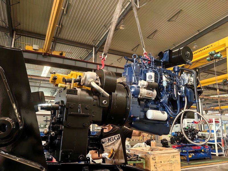 Engine being lifted by overhead crane for installation — backhoe loader