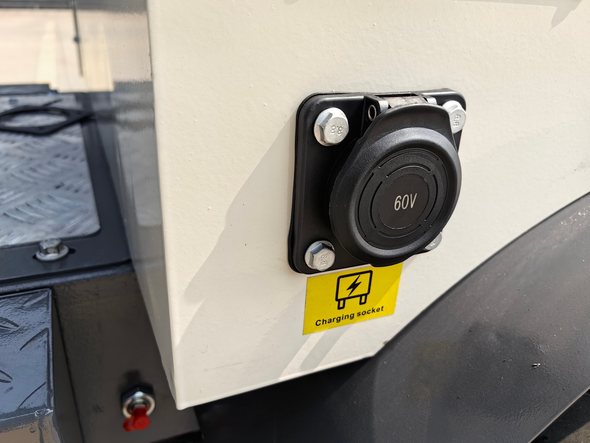 Close-up of the charging socket on a BL 15-06 electric mini backhoe loader — a round 60V connector cover on the white body panel, with a yellow Charging socket label below it